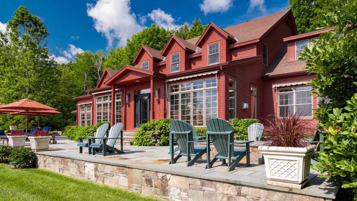 A home painted red with lots of windows and adirondack chairs on a front patio shown on a sunny day in summer
