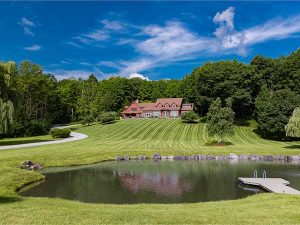 A Vermont home with a lawn and pond in the foreground and trees behind
